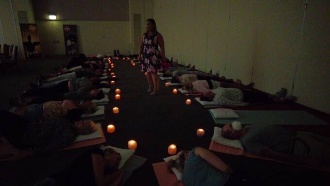 A group of people lying on yoga mats in a dark room with a candle on the floor above their heads