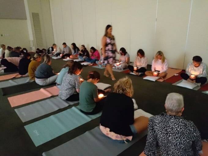 A group of people sitting on yoga mats each holding a candle